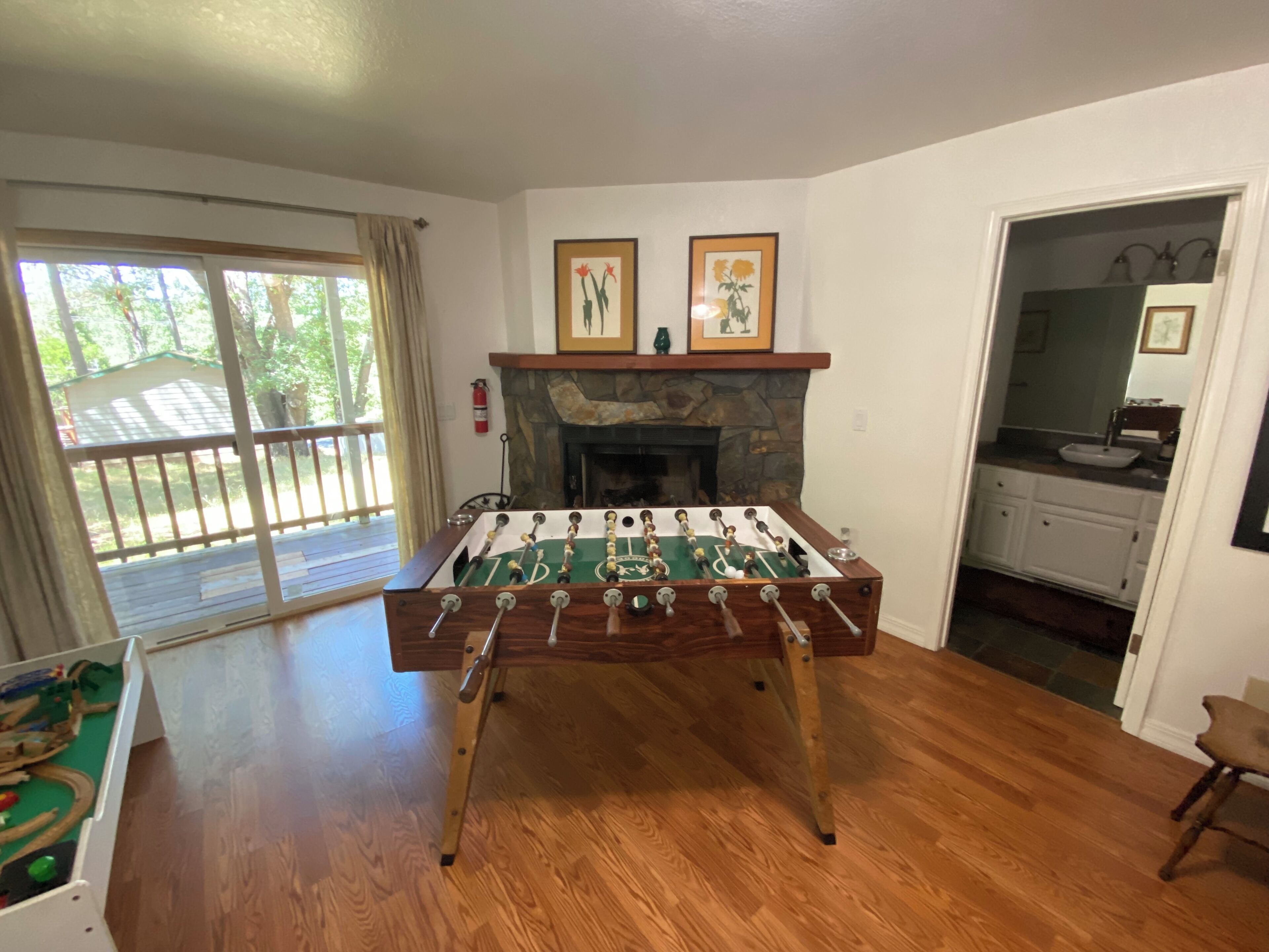 A room with a foosball table, a fireplace, and a view through a glass door to an outdoor deck.