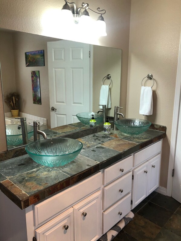 A bathroom with a glass bowl sink, a white door, a towel ring, and a mirror above the sink.
