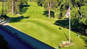 Ein Golfplatz mit einer Fahne, Bäumen und blauem Himmel.