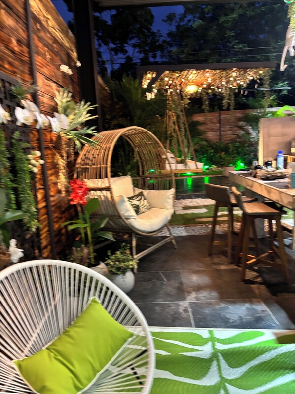An outdoor patio area with a wicker chair, a dining table, and a hanging chair.