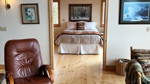 A bedroom with a bed, a wooden floor, a brown leather chair, a wooden bench, and a framed picture on the wall. - LUTSEN LAKEHOUSE on LAKE SUPERIOR (Lutsen)