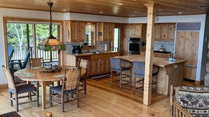 A spacious kitchen with wooden cabinets, a central island, and a dining area with rustic chairs. - LUTSEN LAKEHOUSE on LAKE SUPERIOR (Lutsen)