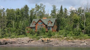 A cabin with a gabled roof, surrounded by dense forest and a rocky shoreline. - LUTSEN LAKEHOUSE on LAKE SUPERIOR (Lutsen)