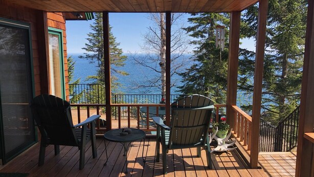 A wooden deck with two chairs and a small table, overlooking a body of water and trees. - LUTSEN LAKEHOUSE on LAKE SUPERIOR (Lutsen)
