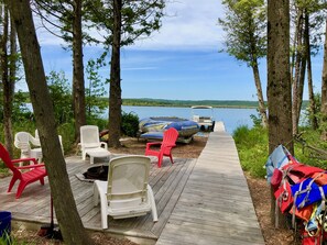 Une terrasse en bois avec des chaises, un bateau et une jetée qui s’avance dans un lac.