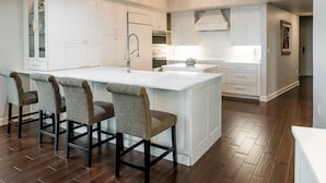 A modern kitchen with white cabinetry, a large island with bar stools, and a chandelier.