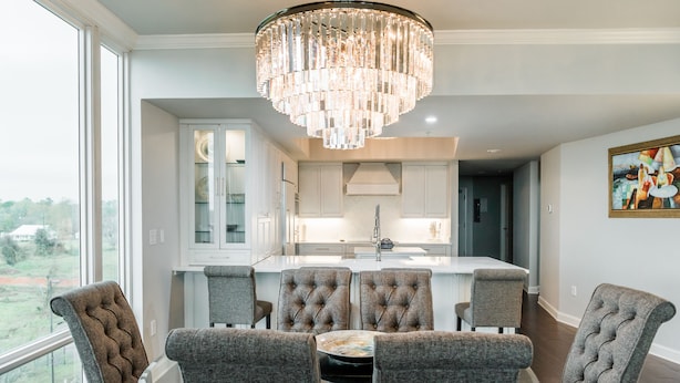 A dining area with a central island, tufted chairs, and a chandelier.