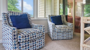 Two patterned armchairs with blue cushions, a wicker chair, and a view of a house through large windows. - 3BR Lewes Condo Near Beaches | 2 Kings + Screened Porch (Lewes)
