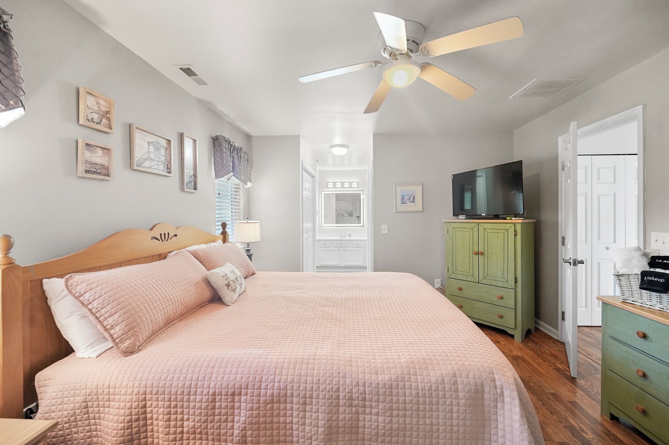A bedroom with a bed, a ceiling fan, a TV, a wardrobe, and a door.