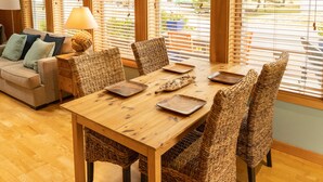 Un coin repas avec une table en bois et des chaises en osier, un canapé avec des coussins et une lampe.