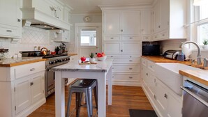 A spacious kitchen with white cabinetry, a central island with stools, a stove, and a microwave. - Hygge Harmony- Salt Hot Tub, 2 Fireplaces, 100+mbps Wifi, AC, Walk to Galveston! (Bend)