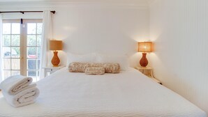 A large bed with white linens, two bedside lamps, and a stack of towels. - Hygge Harmony- Salt Hot Tub, 2 Fireplaces, 100+mbps Wifi, AC, Walk to Galveston! (Bend)