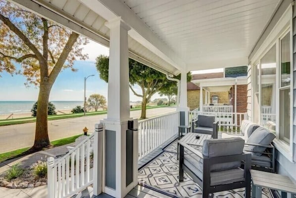 A covered porch with outdoor seating, a view of the beach, and a brick wall.