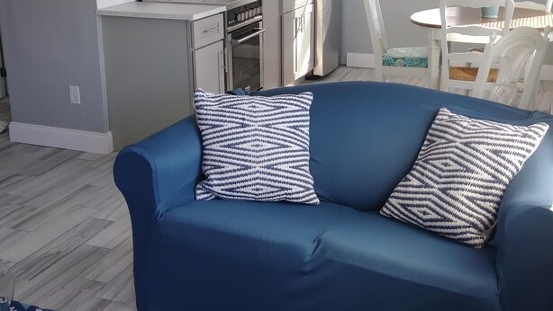 A compact living space with a blue sofa, patterned rug, and a kitchen area with white cabinets and stainless steel appliances.