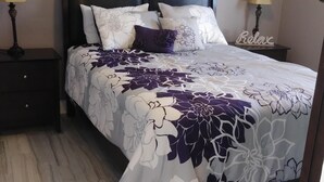 A neatly made bed with a floral bedspread, two bedside tables with lamps, and a 'Relax' sign on the wall.