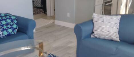 Una sala de estar con dos sofás azules, un tapete estampado y una mesa de centro de vidrio.