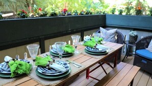 A wooden deck with a table set for four, surrounded by greenery and a blue sky. - Iconic Prospector Condo at Warm Springs (Ketchum)