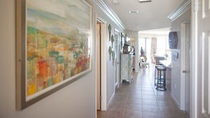 Un passadís amb un quadre abstracte gran a l'esquerra, una porta amb una aldra decorativa i una zona de bar amb tamborets a la dreta.