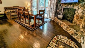 A cozy living room with a stone fireplace, wooden dining table, and a television mounted on the wall. - Charming 3-Bedroom, 2-Bath Townhouse at Snow Summit Base – Ski, Hike, Relax! (BIG BEAR LAKE)