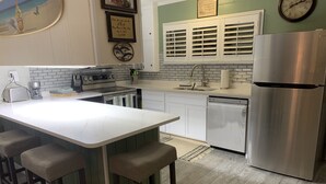 Une cuisine moderne dotée d’un îlot central, de tabourets de bar, d’un réfrigérateur en acier inoxydable et d’un lave-vaisselle.