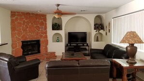 A living room with a stone fireplace, a flat-screen TV, leather sofas, and a ceiling fan.