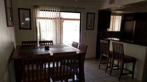 A dining area with a large wooden table and chairs, a kitchen area with a counter and cabinets, and a window with curtains.
