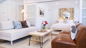 Ett modernt och väl upplyst vardagsrum med en vit soffa, en brun lädersoffa, ett träbord och en säng med ett trägavelt.