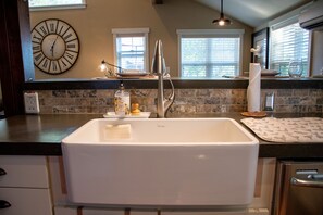 A kitchen with a white sink, a clock, and a window with blinds. - The Barn on Braden, Classic Splendor on the South Side  (Walla Walla)