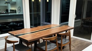 Un coin repas avec une table et des chaises en bois, de grandes fenêtres et une vue sur la cuisine.
