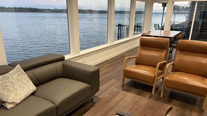Un salon moderne doté d’une grande fenêtre donnant sur un plan d’eau, d’un canapé en cuir marron et d’une table basse en bois.