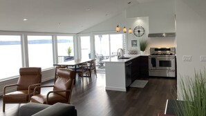 Une cuisine moderne dotée d’appareils électroménagers en acier inoxydable, un coin repas avec une grande table et des chaises, et une vue sur l’eau.