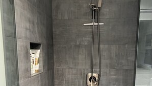 A modern shower with a glass enclosure, grey tiles, and a built-in shelf with toiletries.