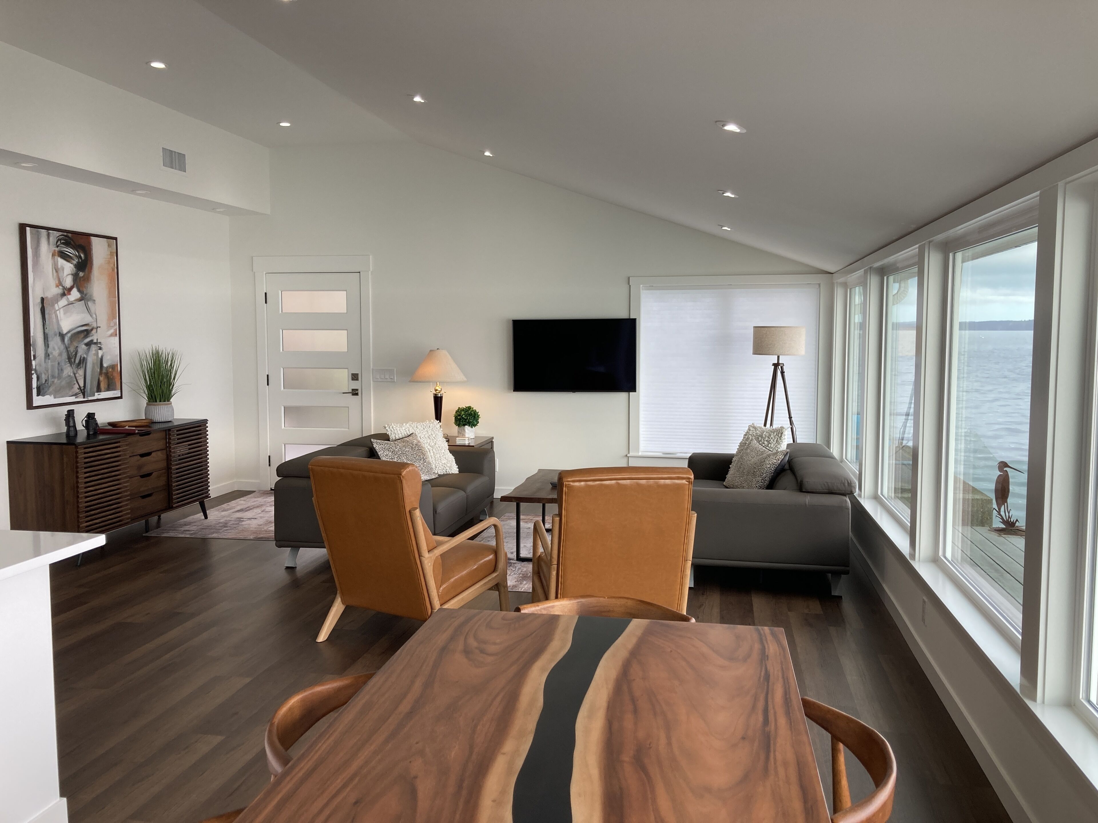 A modern living room with a wooden dining table, two sofas, and a TV.