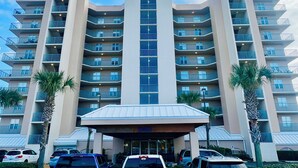 A multi-story hotel with a central entrance, balconies on each floor, and a parking area in front. - Fall Steal! 129/nt base! Gulf front, Pool,Huge Balcony,Beach Supplies,VIEW! (Gulf Shores)
