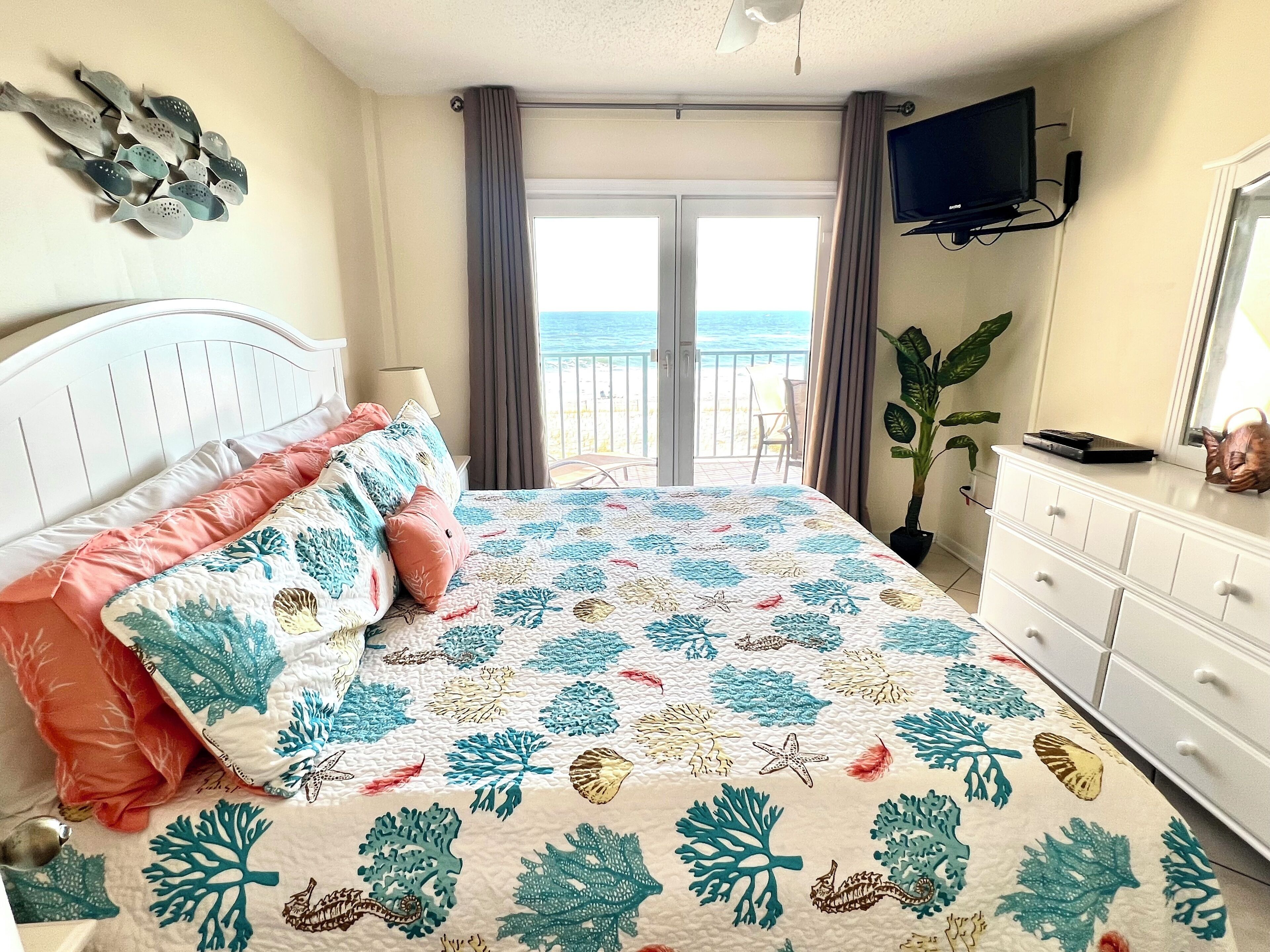 A bedroom with a bed, a dresser, a TV, and a view of the sea.