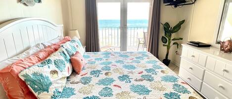 A bedroom with a bed, a dresser, a TV, and a view of the sea.