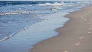 A beach with waves gently lapping at the shore, footprints in the sand, and a clear sky. - Fall Steal! 129/nt base! Gulf front, Pool,Huge Balcony,Beach Supplies,VIEW! (Gulf Shores)