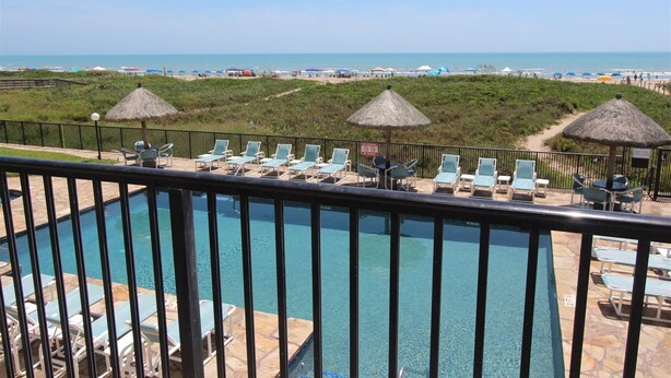 Ein Poolbereich mit Liegestühlen und Sonnenschirmen mit Blick auf Strand und Meer.