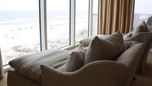 A room with a large window overlooking a beach, a sofa with multiple cushions, and a view of the ocean. - Gorgeous Beach Front Corner Unit with Luxury Designer Updates /Mediterranean @PK (Pensacola)