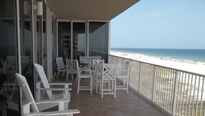 A balcony with white chairs and tables, overlooking a beach with sand and ocean. - Gorgeous Beach Front Corner Unit with Luxury Designer Updates /Mediterranean @PK (Pensacola)