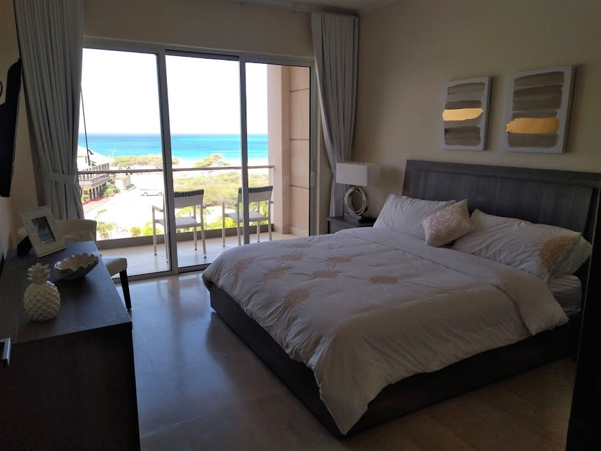 A spacious bedroom with a large bed, a desk, and a view of the ocean through a sliding glass door.