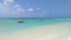 Een strand met helder turquoise water, een zandstrand en twee boten.