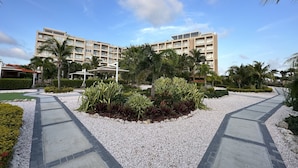 Een hotel met een centraal gelegen binnenplaats, met een grindpad, omringd door palmbomen en diverse planten.