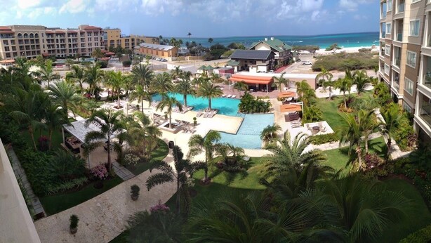 Een resort met een centraal gelegen zwembad, palmbomen en uitzicht op de oceaan.