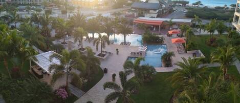 A resort with a large pool, palm trees, and a view of the ocean.