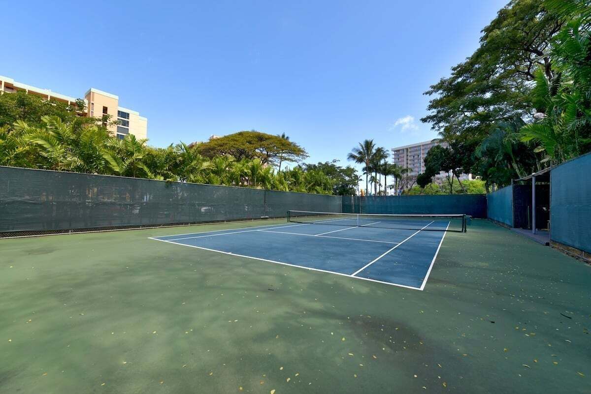 Una cancha de tenis al aire libre rodeada de vegetación y edificios.