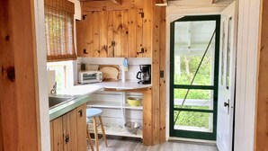 Een kleine keuken met houten kastjes, een inbouwtoaster, een koffiezetapparaat en een raam met uitzicht op groen.