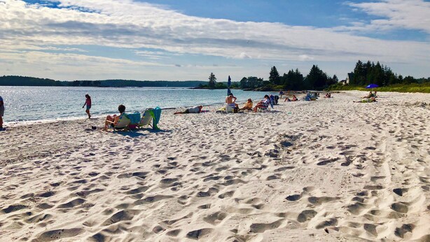 Een zandstrand met mensen die zonnebaden en zwemmen.