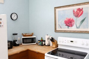 A kitchen with a microwave, stove, toaster, and a clock on the wall.