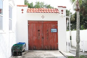 A red wooden gate with a 'Welcome' sign, a white wall, and a green dumpster labeled 'City Gulfport' in front. - Waterfront 1BR Retreat w/Shared Private Beach + Walk to Beach Blvd (Gulfport)